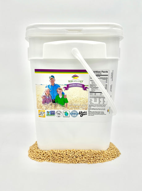 A white plastic bucket labeled with the product name and an image of wheat berries, indicating that it contains 23 lb of soft white wheat berries which are non-GMO, kosher, chemical-free, and have a 25-year shelf-life.